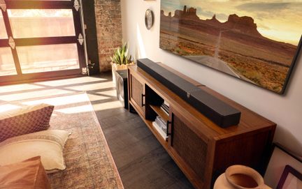 Bară de sunet neagră cu subwoofer lângă un mobilier TV din lemn într-un living luminos cu stil industrial