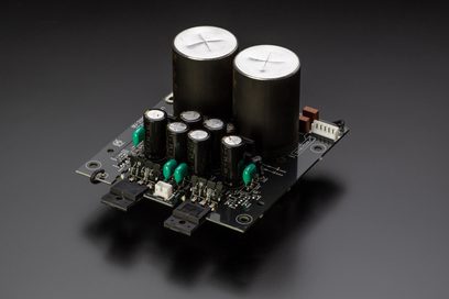 Black printed circuit board with two large silver capacitors, several small green capacitors, and brown resistors