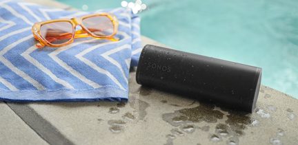 Altavoz portátil negro Sonos, toalla azul con patrones blancos, gafas de sol naranjas, borde de piscina