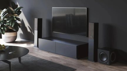 Čierna zostava domáceho kina s dvoma stĺpovými reproduktormi a subwooferom vedľa televízora zaveseného na stene
