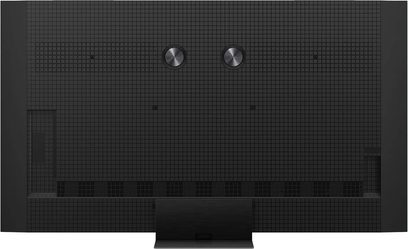 TCL 85C9K høyoppløselig TV i matt svart plast, baksidevisning som viser et rutet panel, to sirkulære metallskiver øverst, ventilasjonsrister nederst og et sentralt rektangulært stativ