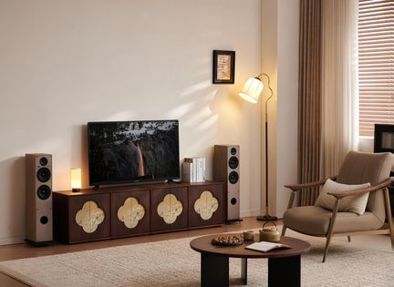 Obývací pokoj, TV stolek z tmavého dřeva s květinovými panely, černý televizor, béžové reproduktory, stojací lampa, křeslo