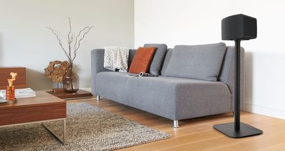 Lys grå hjørnesofa, dekorative puder, træbordplade, vase med grene, beige tæppe, sort højttalerfod