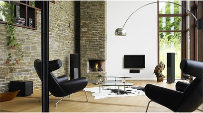 Moderne stue med sorte sofaer, buet lampe, pejs og store vinduer, sorte Jamo S 608 gulvhøjttalere på hver side
