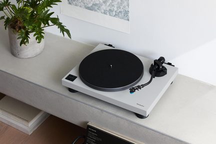 Grå mat vinylplade set i trekvarts perspektiv, sort drejeskive med filtunderlag, tonearm, betjeningsknapper til venstre