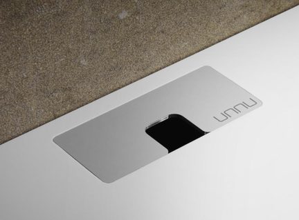 Stříbrná kovová destička s černým centrálním otvorem a logem „unnu“, na bílém podstavci, šikmý pohled shora