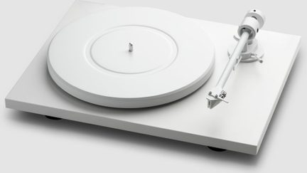 Hvid pladespiller i metal og plast med mat finish, set skråt ovenfra med rektangulær sokkel, cirkulær pladetallerken og sideplaceret tonearm