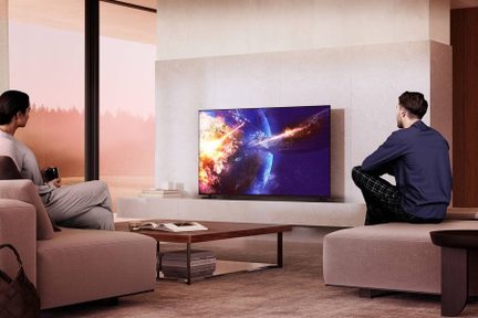 Nowoczesny, beżowy salon; z przodu czarny telewizor z płaskim ekranem na niskiej szafce RTV, drewniany stolik kawowy, na ekranie scena kosmiczna