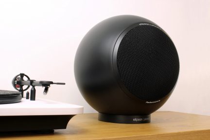Un altoparlante sferico nero con una griglia in metallo e un giradischi bianco con un braccio nero su una superficie in legno