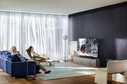 Moderne stue med blå sofa, beige lænestole, gråt tæppe, Samsung QE55Q800T-tv der viser et snelandskab og skov