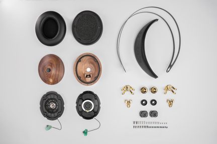 Casque audio démonté vu de dessus, coussinets noirs en cuir, coques en bois brun, arceau métal noir, pièces et vis dorées