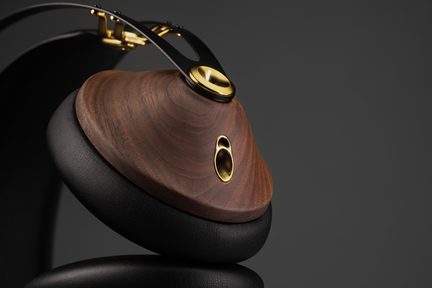 Gros plan d’un casque audio, oreillette en bois brun avec inserts dorés, arceau noir en métal, coussinet en cuir noir