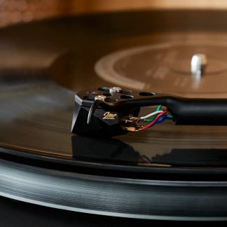 Cellule et bras noirs en métal d’une platine vinyle, câbles colorés visibles, gros plan en vue de côté sur disque noir