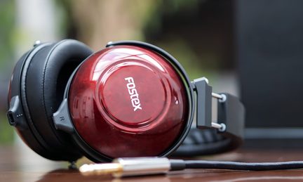 Et hovedtelefon med skinnende røde ørepuder med "Fostex"-logoet, en sort bøjle og et kabel med et forgyldt stik