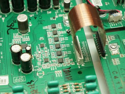 Grønt printplade med kobberfarvede elektroniske komponenter såsom kondensatorer og spole, tæt på udsigt over indersiden af en elektronisk enhed