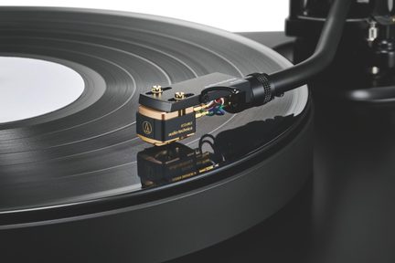 Primo piano di una testina phono nero e oro in metallo audio-technica, cavi colorati, su un disco in vinile nero