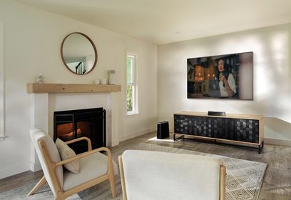 Moderne stue med hvid sofa, beige lænestol, tæppe med mønstre, træ-TV-møbel og fladskærm, der viser en smilende kvinde