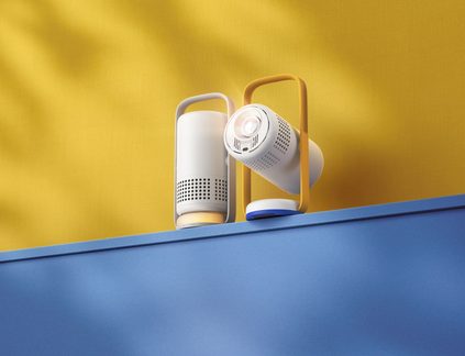 Dva malé válcové projektory z bílého plastu, ventilační mřížky, žlutá madla, na modrém okraji