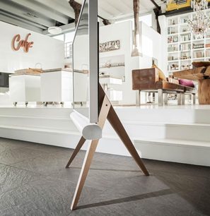 Designmøbel til TV i form af en trebensstol i lyst træ og hvid farve i et moderne indendørsmiljø med bogreol og "Café"-dekoration