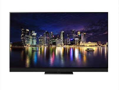Panasonic TX-77MZ2000E-fladskærm, der viser et natligt vue af oplyste skyskrabere, der spejler sig i vandet