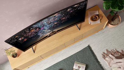 Televizor Samsung UE65RU7305 zobrazující obraz barevných ohňostrojů na světlém dřevěném nábytku s rostlinami a dekorativními předměty