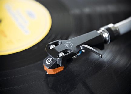 Černá a oranžová přenoska Audio-Technica na raménku gramofonu přehrávajícím černou desku se žlutým štítkem