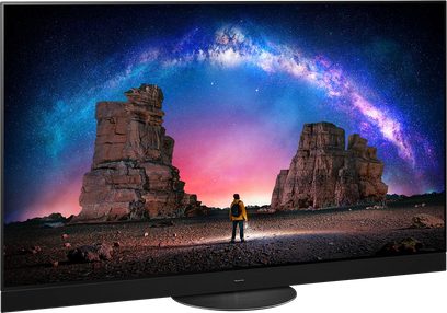 Téléviseur Panasonic TX-65MZ2000E affichant une image de rochers géologiques sous un ciel étoilé avec une arche galactique colorée et une personne debout devant