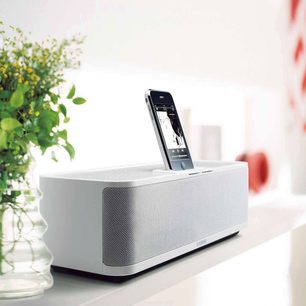 Bílý dokovací stojan Yamaha PDX-31 zepředu, vložený iPhone, vlevo zelené rostliny, bílé pozadí