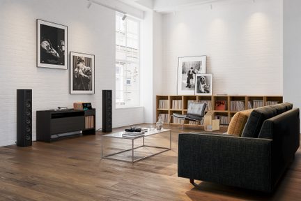 Moderne, lyst stue med grå sofa, sofabord i metal og glas, reol med vinylplader og sorte gulvhøjttalere