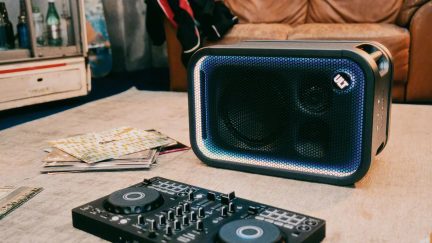 Svart Ultimate Ears bærbar høyttaler med blå LED-belysning, plassert på et bord nær en DJ-konsoll