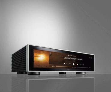 Leitor de áudio em rede Rose RS130 prata visto de frente, tela LCD exibindo "Ultimate Network Transport", painel frontal em alumínio escovado