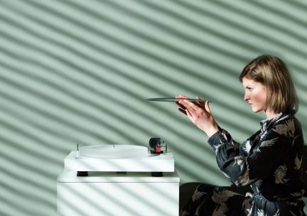 Kvinne som holder en vinylplate over en hvit platespiller, sett fra siden