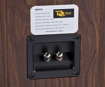 Kompakt Davis Acoustics Maya højttaler i valnøddetræ, med synlige højttalere bag et sort gitter og hvid teknisk etiket