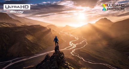 Silhouette of a person standing on a rock overlooking a mountainous valley at sunset, winding river below