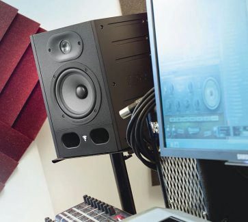 Sort studiemonitor set forfra, med synlige højttalere, omgivet af et tastatur, en mus og en bærbar computer