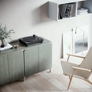 Pickup pentru discuri de vinil Technics SL-100CEG-K negru pe un mobilier din lemn deschis la culoare, într-un interior modern minimalist și luminos