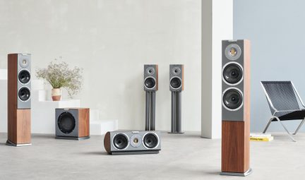 Hi-fi-højttalersæt bestående af to gulvhøjttalere, to standerhøjttalere, en centerhøjttaler og en subwoofer, rektangulære kabinetter i brun træfinér og grå metalfront med sorte runde højttalerenheder, set i perspektiv