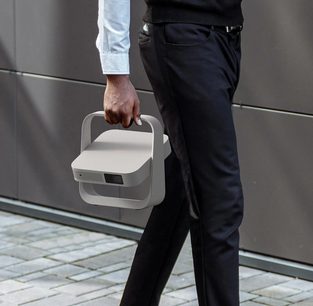 XGIMI Elfin Flip, zijaanzicht, vastgehouden aan een handvat, gedragen door een persoon in een zwarte broek en een wit overhemd, grijze achtergrond