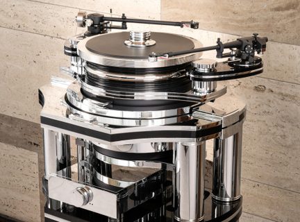 Prato de vinil preto e prateado em metal polido e acrílico, equipado com dois braços de leitura, um prato circular elevado e pilares cilíndricos cromados, vista de três quartos frontal