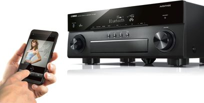 Yamaha RX-A850 sort hjemmebiografsforstærker, frontpanel med LCD-skærm, knapper og stik, hånd der holder en smartphone
