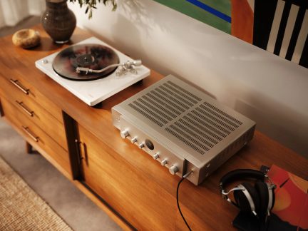 Stříbrný stereo zesilovač Marantz s bílým gramofonem a sluchátky na dřevěném nábytku