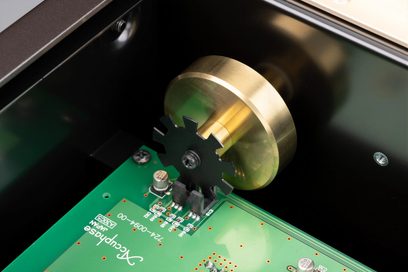 Primo piano interno del sintonizzatore Accuphase T-1300, disco in ottone dorato, ruota dentata nera, scheda verde, vista obliqua