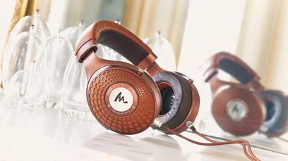 Lukket hi-fi hovedtelefon Focal Stellia i brunt læder og kobbermetalfarve, set fra siden, liggende på et hvidt, gennemsigtigt stofmateriale