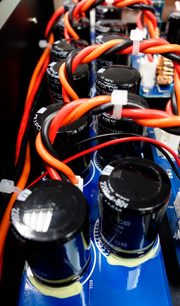 Flere sorte og orange elektrolytiske kondensatorer forbundet med røde elektriske ledninger på et blåt printplade