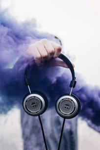 Grado SR325x avoin kuuloke kädessä pilvistä taivasta vasten, lähikuva edestä