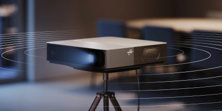 Videoproiettore ALPD grigio e nero su treppiede, vista di tre quarti, fascio luminoso acceso in interno