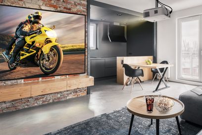 Moto amarilla estacionada en una sala de estar moderna con cocina abierta, mesa de centro redonda de madera y dos sillas negras