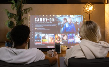 Videoproiettore portatile che mostra Netflix su grande schermo in un soggiorno, due persone sedute di spalle