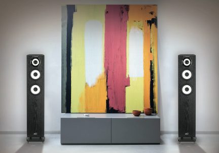 Two black speakers with three white drivers each, a gray cabinet, three brown bowls, a colorful abstract painting.