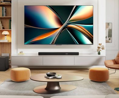 Salon modern, TV cu ecran plat montat pe perete cu ramă subțire, mobilier jos alb lăcuit cu bară de sunet neagră, masă de cafea ovală din metal